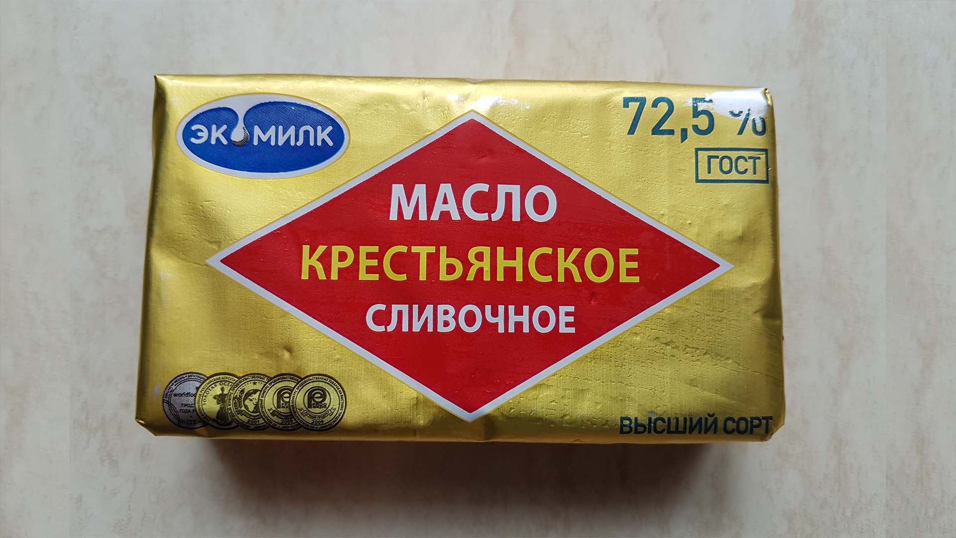 Сливочное масло "экомилк, крестьянское 72,5%" в упаковке на кухонном столе.